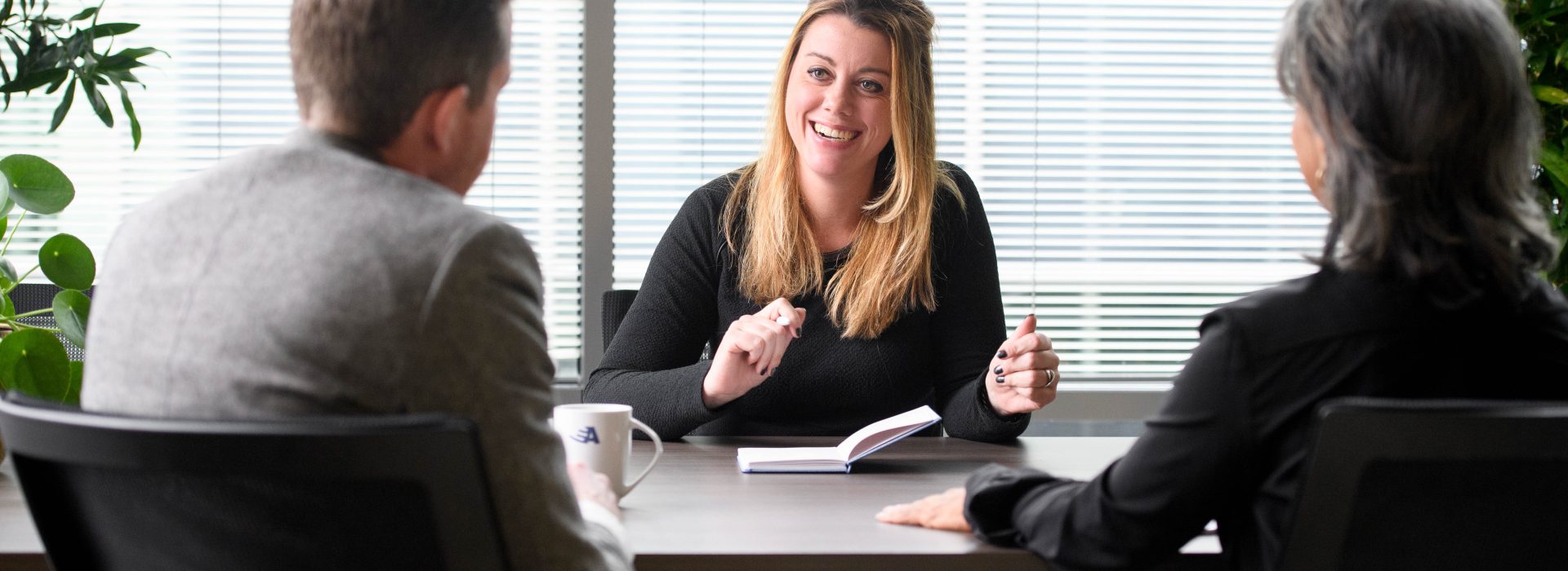 Drie managers zitten aan tafel, met elkaar in gesprek