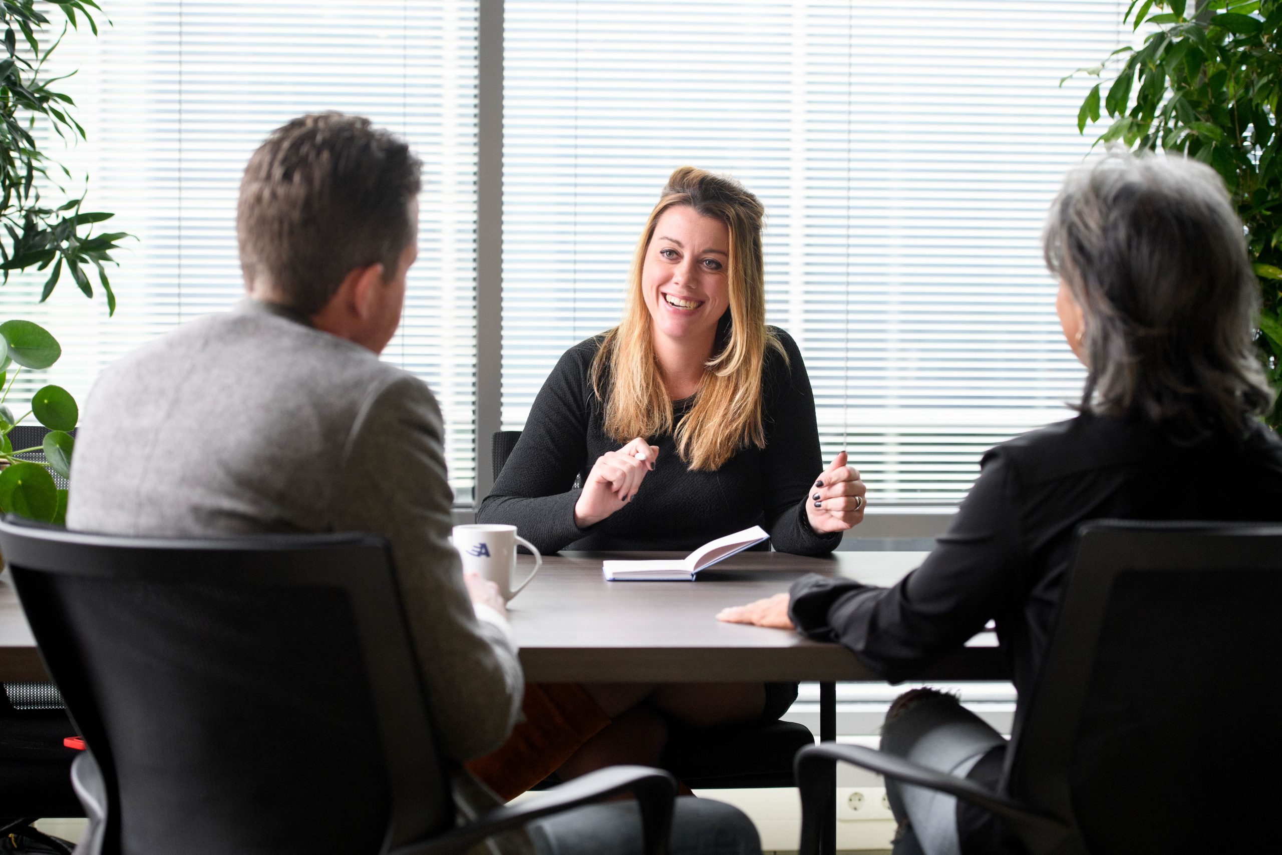 Drie managers zitten aan tafel, met elkaar in gesprek