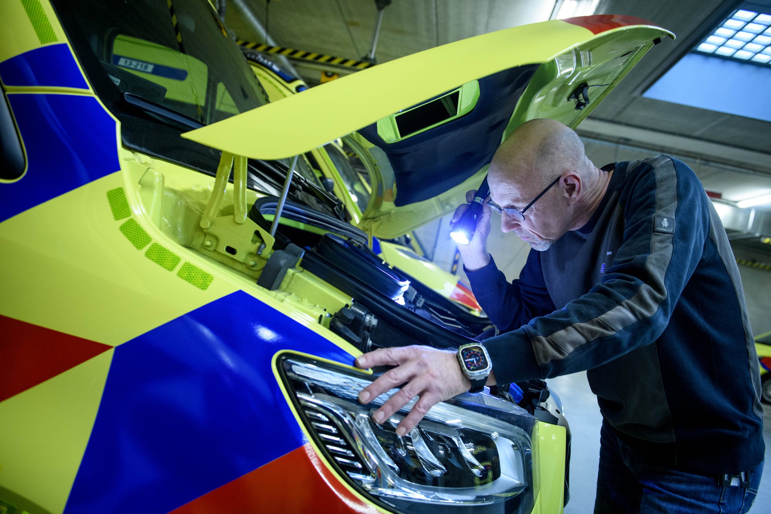 Een facilitair medewerker is met behulp van een zaklamp onder de motorkap aan het inspecteren