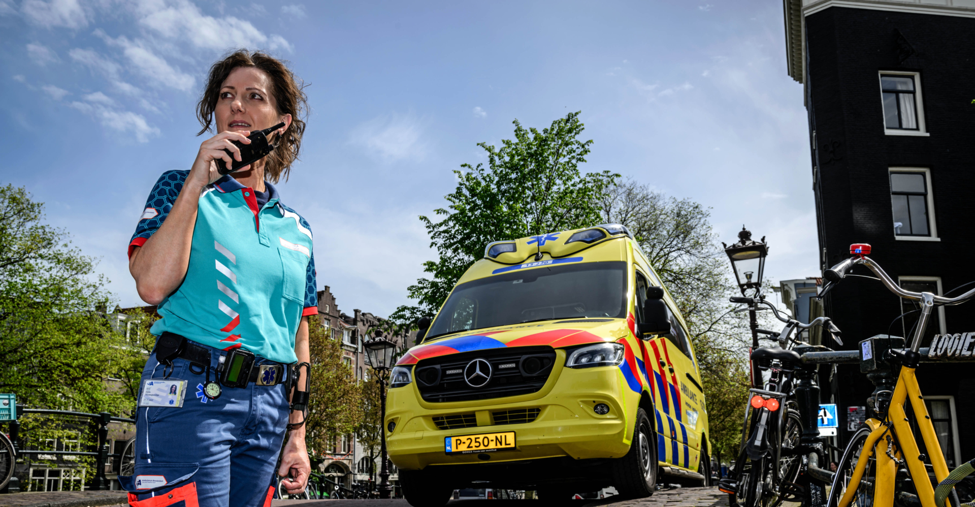 Verpleegkundige middencomplexe ambulance praat door de portofoon met de meldkamer. ambulancezorg. Ze staat midden in Amsterdam, op een brug over de gracht, voor de ambulance