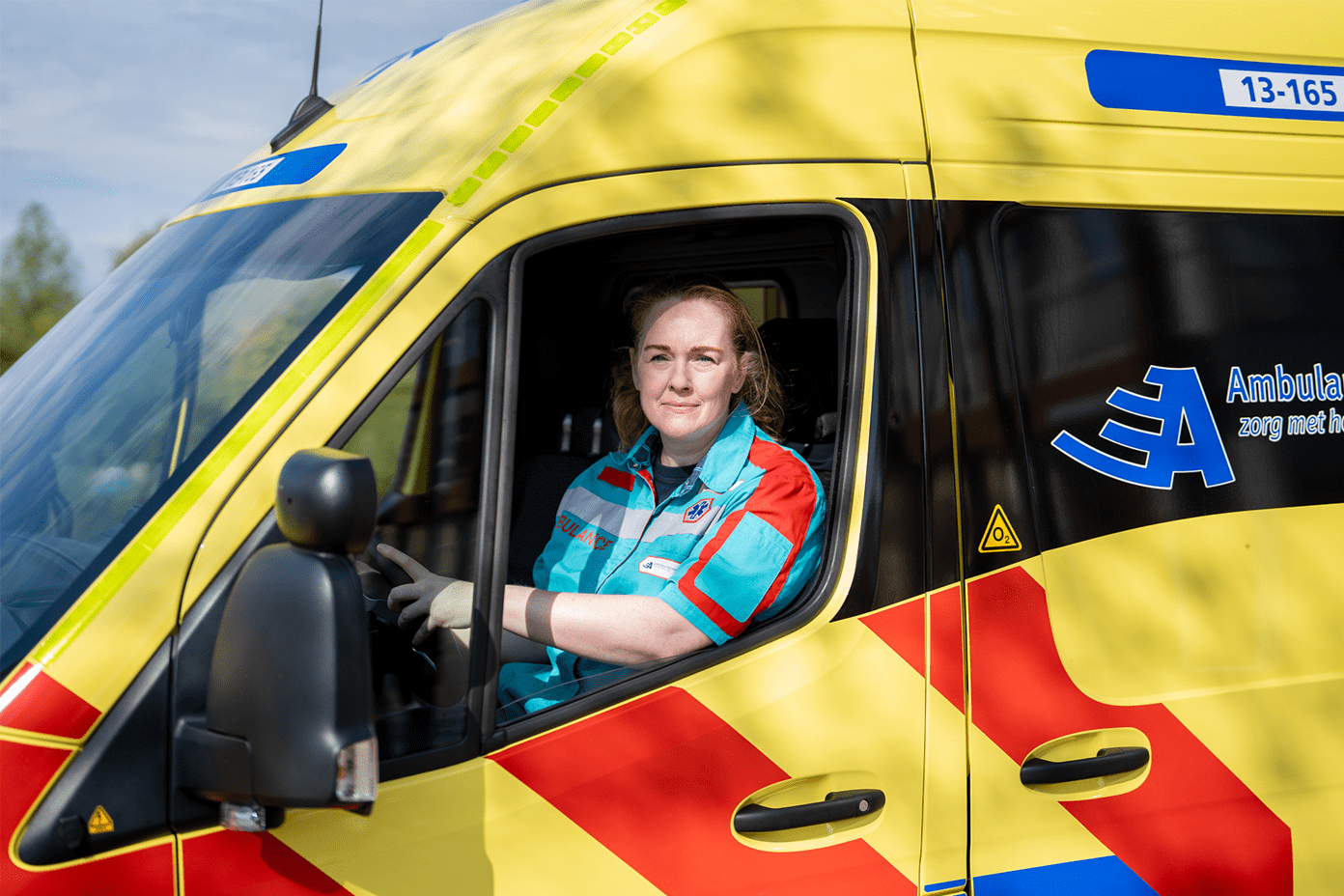 Ambulancechauffeur zit in de ambulance achter het stuur. Ze kijkt uit het raam.