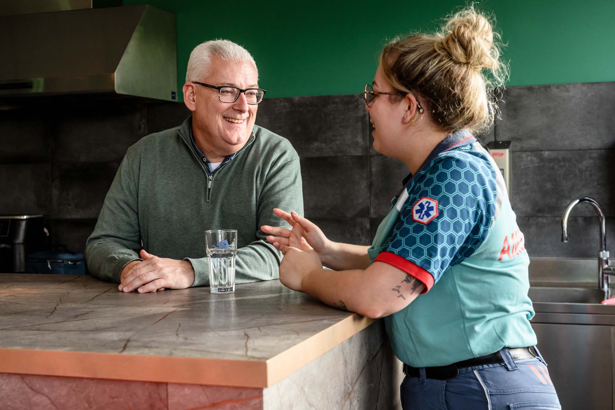 Medewerker ambulance in gesprek met kantoormedewerker in keuken